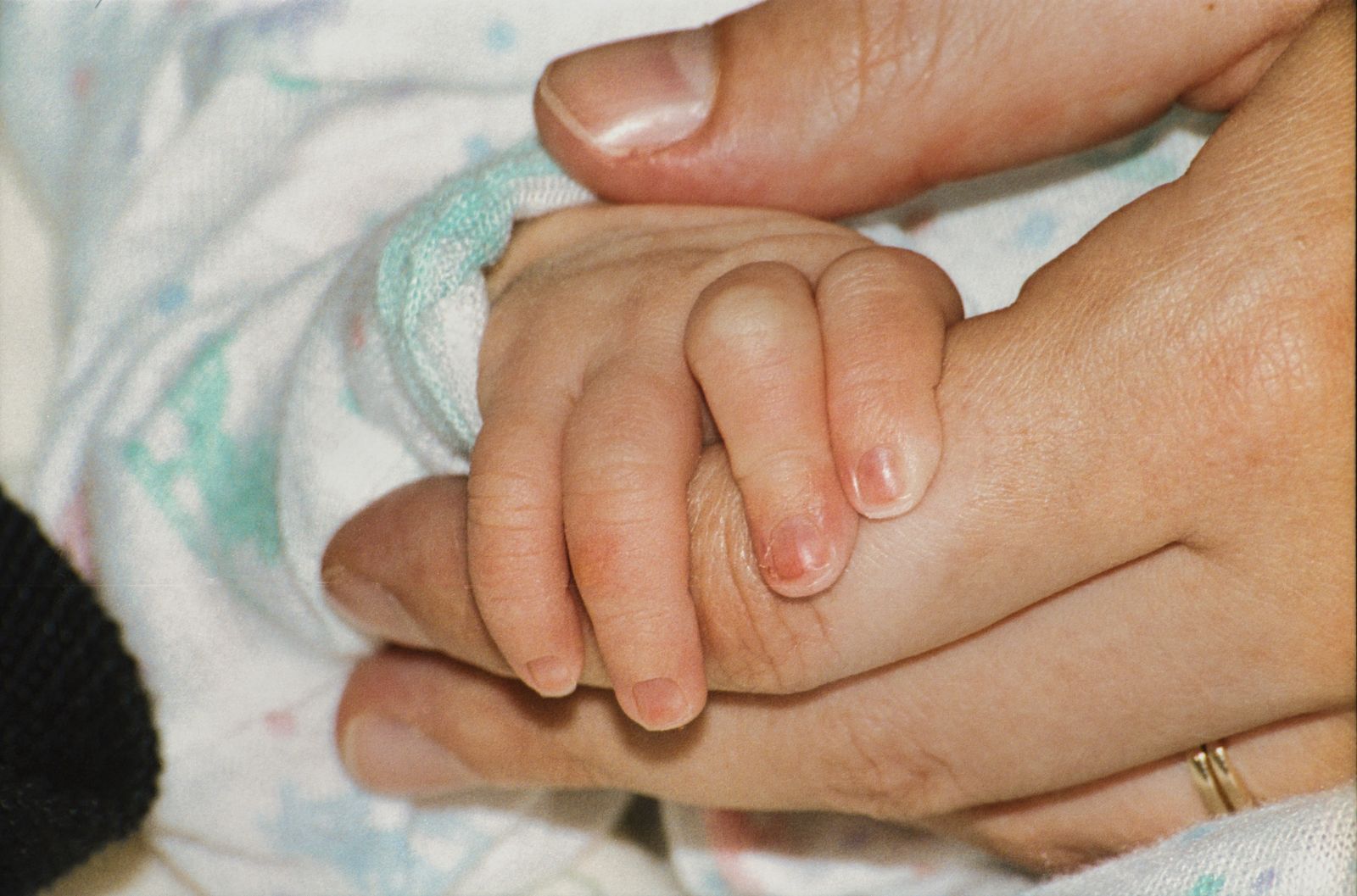 A baby’s small hand holding an adult’s thumb