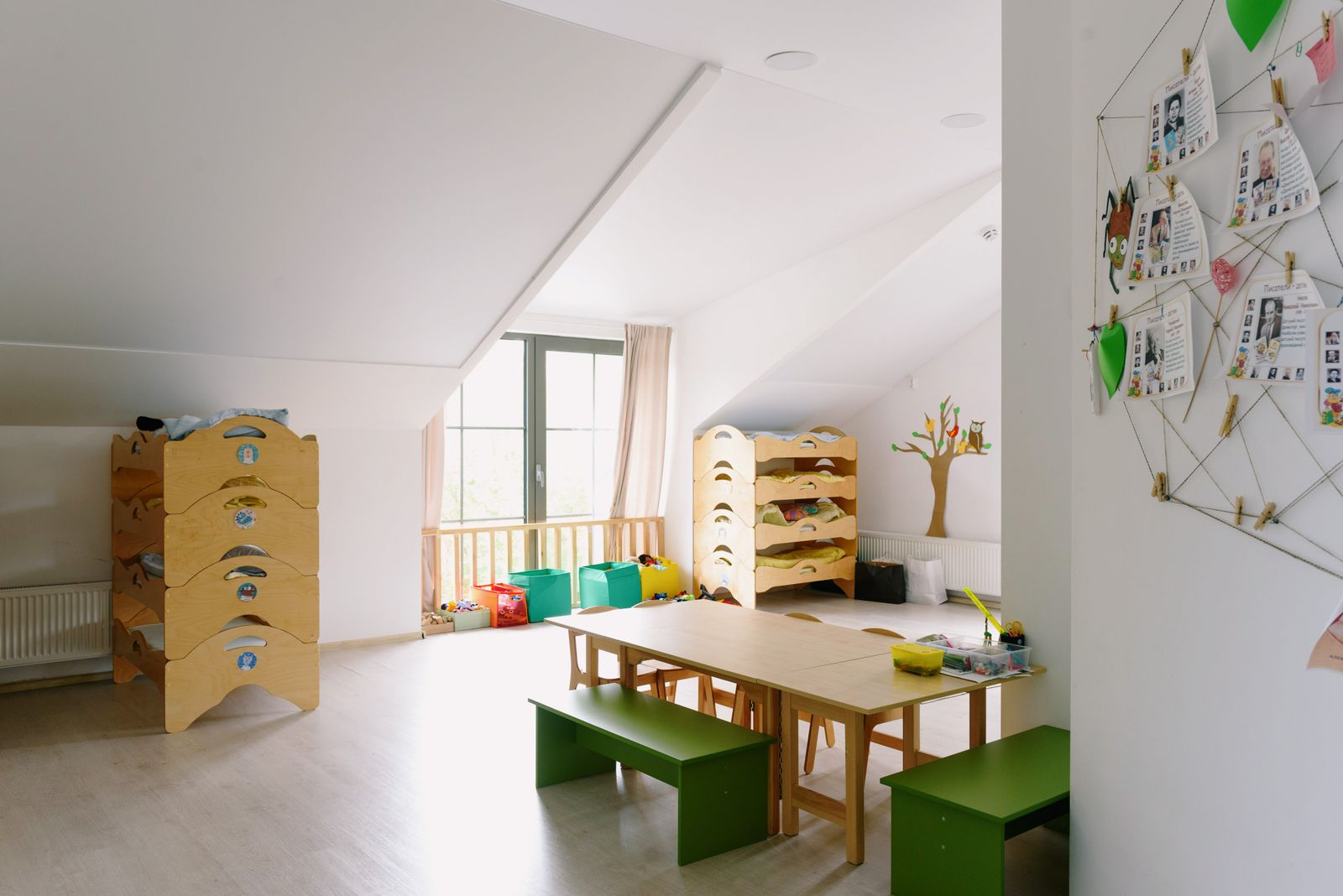 A room with a sloped ceiling, a wooden table, green benches and low shelves of toys under a window