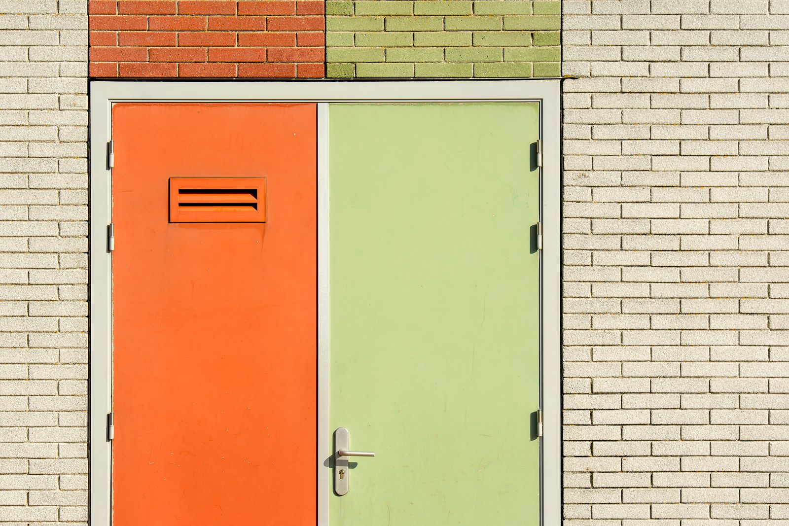 An orange door and a green door side by side in a pale brick wall