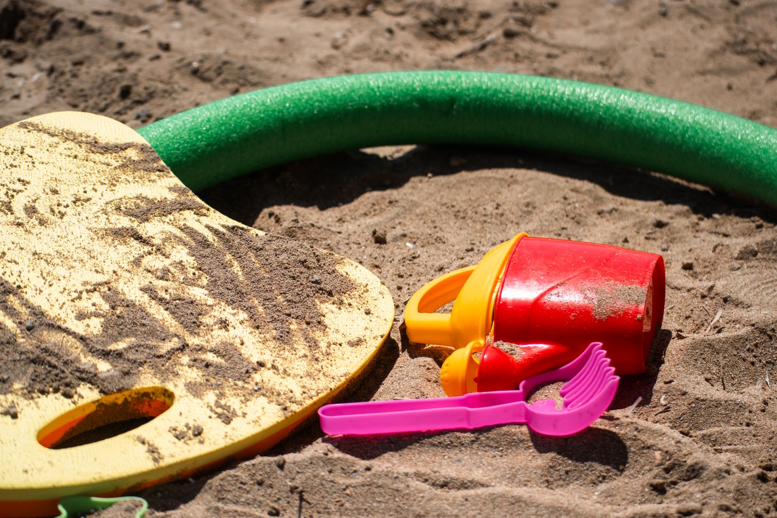 A red sand bucket and a pink shovel in a sandbox