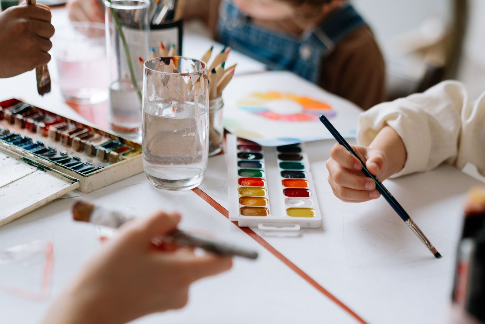 Hands holding brushes over a watercolor set and jars of water